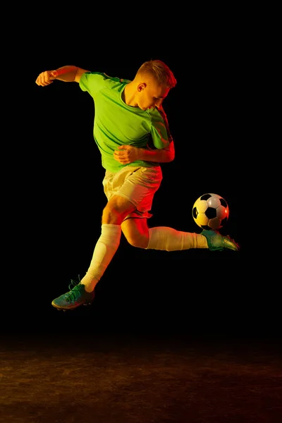 Goal. Young soccer, football player in motion and action with ball isolated on dark background in neon light. Concept of art, creativity, sport, energy. Copy space for ad, text
