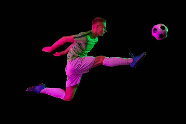 体育在行动 一名职业足球运动员在霓虹灯滤光片中以黑暗背景隔离的足球进行训练 力量和精力 精力充沛的运动员练习 — 图库照片