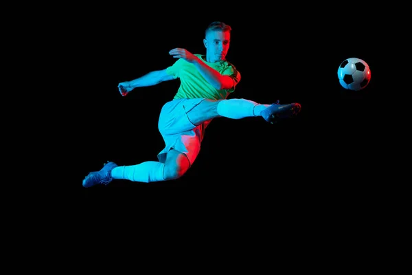 スポーツ活動中 ネオンライトフィルターの暗い背景に隔離されたサッカーボールと1人のプロサッカー選手のトレーニング スポーツ スピード パワーとエネルギー エネルギー運動選手 — ストック写真