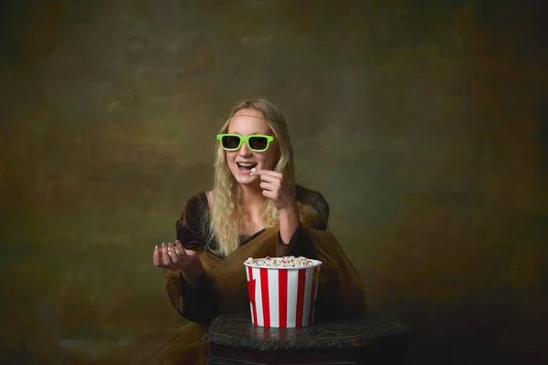 Comedy. Cheerful young girl in image of Mona Lisa in 3d eyewear wathich movie over dark vintage background. Retro style, art, fashion, comparison of eras concept.