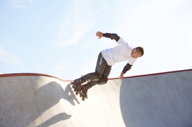 Halka açık kaykay parkında yetişkin erkek paten eğitimi. Adam zıplama, numaralar yapıyor. Aktif yaşam tarzı, spor, hareket, hobiler. Sonbahar güneşli bir günde dışarıda boş zaman aktiviteleri.