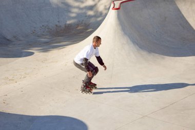 Halka açık kaykay parkında yetişkin erkek paten eğitimi. Adam zıplama, numaralar yapıyor. Aktif yaşam tarzı, spor, hareket, hobiler. Sonbahar güneşli bir günde dışarıda boş zaman aktiviteleri.