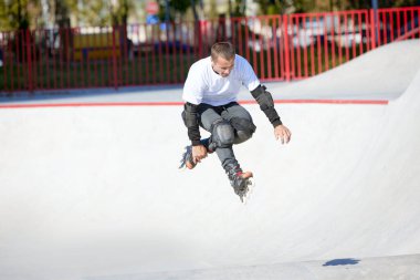 Halka açık kaykay parkında yetişkin erkek paten eğitimi. Adam zıplama, numaralar yapıyor. Aktif yaşam tarzı, spor, hareket, hobiler. Sonbahar güneşli bir günde dışarıda boş zaman aktiviteleri.