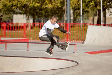 Halka açık kaykay parkında yetişkin erkek paten eğitimi. Adam zıplama, numaralar yapıyor. Aktif yaşam tarzı, spor, hareket, hobiler. Sonbahar güneşli bir günde dışarıda boş zaman aktiviteleri.