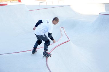 Halka açık kaykay parkında yetişkin erkek paten eğitimi. Adam zıplama, numaralar yapıyor. Aktif yaşam tarzı, spor, hareket, hobiler. Sonbahar güneşli bir günde dışarıda boş zaman aktiviteleri.