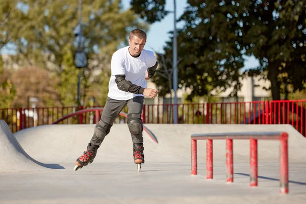 Halka açık kaykay parkında yetişkin erkek paten eğitimi. Adam zıplama, numaralar yapıyor. Aktif yaşam tarzı, spor, hareket, hobiler. Sonbahar güneşli bir günde dışarıda boş zaman aktiviteleri.