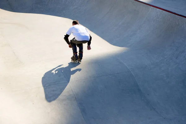 Back view of man on roller skates in motion at modern roller skate park. Professional roller skater doing dangerous and daring tricks. Concept of sport, health, speed, and energy. Leisure time