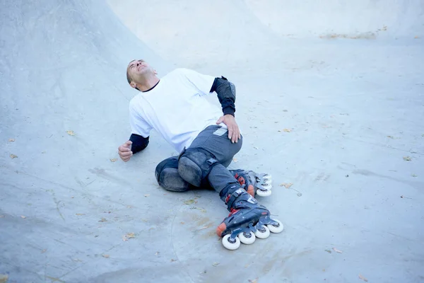 Fall, leg injury. Man on roller skates lying on wooden covering track at skate park. Roller skater did dangerous and daring tricks. Concept of sport, health, speed, and energy. Leisure time