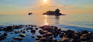 Huzurlu bir körfezde gün batımı gökyüzü ve ıssız bir adaya bakan resim gibi bir deniz manzarası.. 