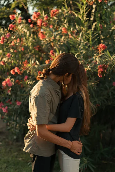 若いです大人カップル屋外抱擁お互いにキス屋外で日没の間に花の背景 — ストック写真