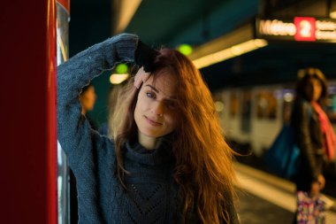 Uzun saçlı bir kadın bir otomatın önünde metro bekliyor.