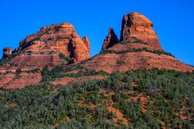 Rock formations surrounding Sedona, Arizona, US. Prominent orange butte, with contrasting green plants and blue sky