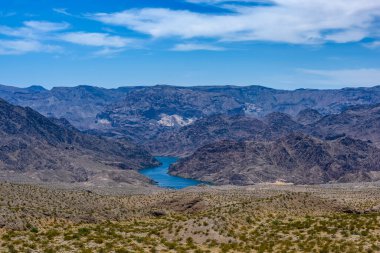 View of the Colorado River bend in Nevada, US. Beautiful blue water and blue sky contrasting with the brown hills around it. Desert plants in the foreground.
