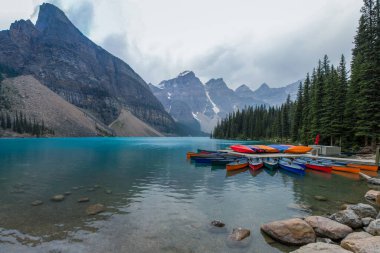 Alberta, Kanada 'daki güzel Louise Gölü. Üzerinde renkli kanolar olan çarpıcı turkuaz mavi su. Arka planda dağlar ve buzullar var. Dramatik, bulutlu gökyüzü.