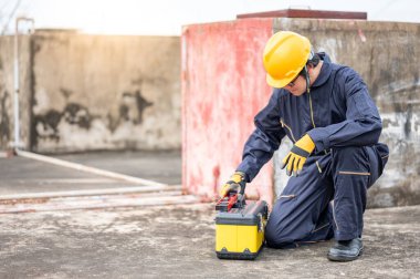 Erkek Asyalı tamirci ya da bakım işçisi koruyucu giysi ve kask giyen inşaat alanında iş aletleri taşıyan bir adam. Makine mühendisliği projesi için ekipman