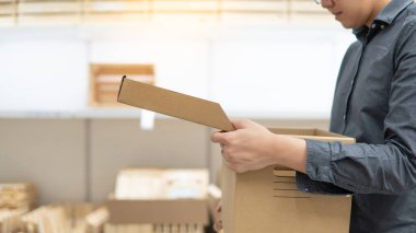 Depodaki ürün raflarının yanında karton kutu kapağı açan genç bir Asyalı. Paket nakliye ve teslimat servisi. Kutuların açılması veya açılması