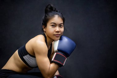 Çekici Asyalı boksör kadın spor salonunda oturmuş mavi boks eldivenleriyle poz veriyor. Kadın boks sınıfı ve dövüş sanatları konsepti