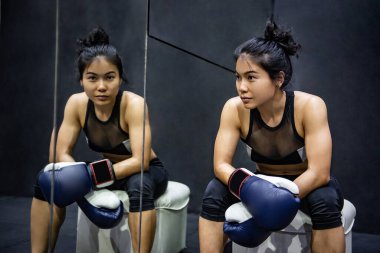 Çekici Asyalı boksör kadın spor salonunda oturmuş mavi boks eldivenleriyle poz veriyor. Kadın boks sınıfı ve dövüş sanatları konsepti