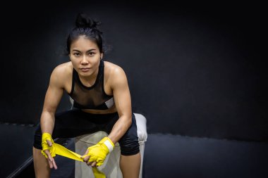 Spor salonunda sandalyede otururken bileğinde sarı pamuklu bandaj olan Asyalı kadın boksör. Kaslı vücutlu atlet kadın boks sporuna hazırlanıyor. Dövüş sanatları konsepti