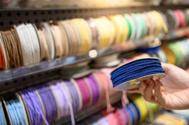 Marketteki renkli kurdele rafından mavi Ric Rac kurdelesini seçen bir erkek. Sanatçı ve El Sanatları konsepti