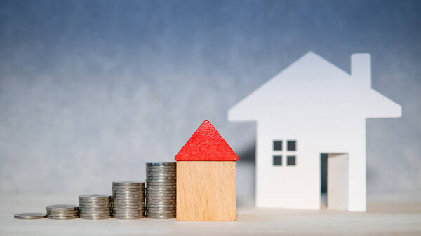 Концепция инвестиций в недвижимость. Ставка по ипотечному кредиту. Копил деньги на будущую пенсию. Деревянная модель дома с монетами на столе
.