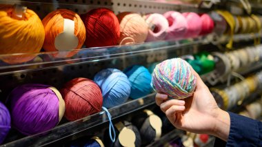 Erkek eli örgü dükkanında ya da dikiş atölyesinde kırmızı iplik topunu seçiyor. Dükkanın önünde renkli yün iplik seçimi var. Alışveriş yaşam tarzı konsepti