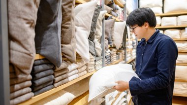 Genç Asyalı müşteri mobilya mağazasında yastık ya da kanepe seçiyor. İç mekan tasarımı için alışveriş evi dekorasyonu. Ev geliştirme kavramı