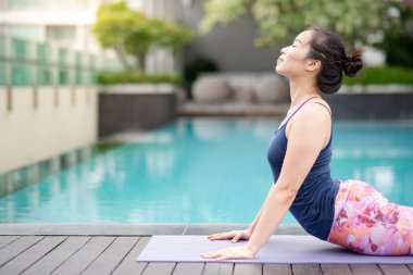 Çekici genç Asyalı kadın Bhujangasana ile yoga egzersizi yapıyor ya da Kobra yüzme havuzunun yanında poz veriyor. Evde idman yapıyorum. Sağlıklı yaşam tarzı kavramı. Uluslararası Yoga Günü
