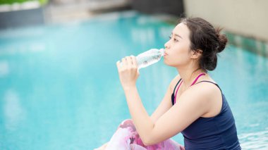 Yüzme havuzunda pilates yaptıktan sonra su içen çekici genç Asyalı kadın. Açık hava egzersizi, sağlıklı yaşam tarzı ve ferahlatıcı kavramlar.