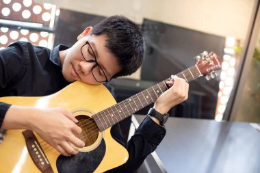 Genç Asyalı gitarist evde klasik gitaristle müzik çalıyor. Eğlence aktivitesi ya da kişisel hobi için telli müzik aleti. Rahatlama ve eğlence kavramları
