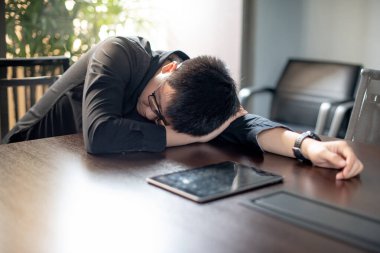 Çok çalışan Asyalı işadamı konferans masasında dijital tabletle ofis toplantı odasında uyuyor. Aşırı çalışma konseptinden kaynaklanan yorgunluk ve sağlık sorunları