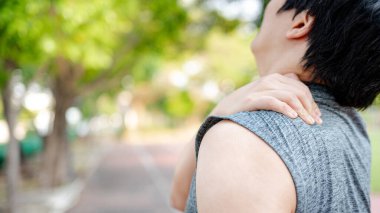 Asyalı sporcu parkta egzersiz yaparken yorgun ve omuz ve boyun ağrısı çekiyor. Spor sakatlığı ya da sağlık konsepti