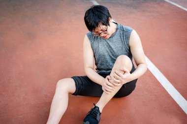 Asyalı atlet, parkta egzersiz yaparken bacak ve diz ağrısından muzdarip baldır krampı geçiriyor. Spor sakatlığı ya da sağlık konsepti