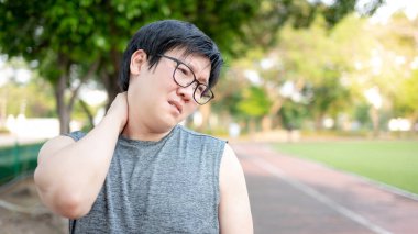 Asyalı sporcu parkta egzersiz yaparken yorgun ve omuz ve boyun ağrısı çekiyor. Spor sakatlığı ya da sağlık konsepti