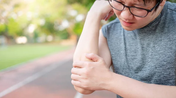Parkta egzersiz yaparken dirsek ve kol ağrısı çeken Asyalı sporcu. Spor sakatlığı ya da sağlık konsepti