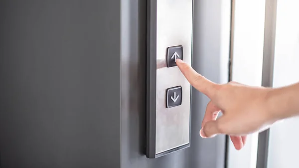 Male forefinger pressing on button up in front of the elevator (lift) in office building. Mechanical engineering concept