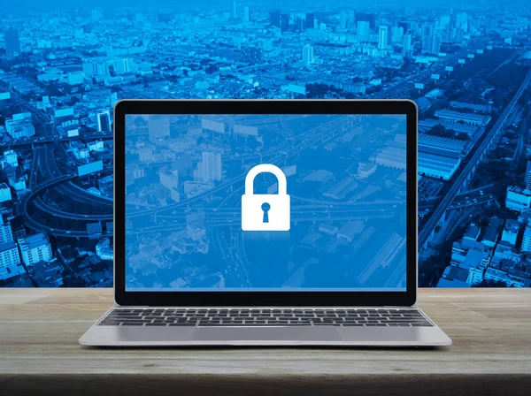 Padlock icon on modern laptop computer monitor screen on wooden table over city tower, street, expressway and skyscraper, Technology internet cyber security and safety online concept