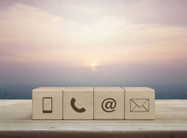 Cep telefonu, telefon, e-posta adresi, ahşap blok küplerindeki posta simgesi şehir kulesinin üzerindeki ahşap masa ve günbatımında gökdelen, klasik tarzda, iş dünyası müşteri hizmetleri ve çevrimiçi konsepti desteklemek.