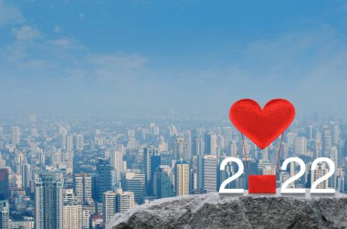 Kırmızı Kumaş Kalp, 2022 beyaz metinli hava balonunu modern şehir kulesi ve gökdelen üzerindeki kaya dağında seviyor. Sevgililer Günü konsepti.