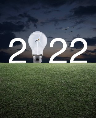 2022 beyaz yazı ve ampul içinde rüzgar türbini olan yeşil çimlerin üzerinde günbatımı gökyüzünde kuşlarla birlikte. Mutlu yıllar 2022 ekolojik kapak kavramı.
