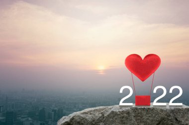 Kırmızı Kumaş Kalp, 2022 Beyaz Metin 'li hava balonuna bayılıyor. Gün batımında şehir manzarasının havadan görünüşü, klasik tarz, mutlu yıllar ve Sevgililer Günü 2022 konsepti.