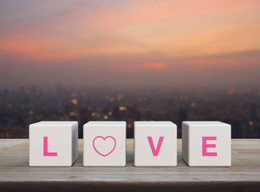 Beyaz blok küpleri üzerinde aşk mektubu ahşap masa üzerinde şehir manzarası bulanık gün batımında, Sevgililer Günü konsepti