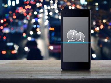 Soru işareti ve bilgi sohbet simgesi ahşap masa üzerinde modern akıllı cep telefonu ekranında bulanık gece lambası trafik sıkışıklığı yolu üzerinde şehir arabaları, iş müşteri hizmetleri ve çevrimiçi konsept destek