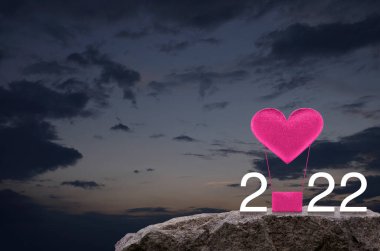 Pembe kumaşlı kalp hava balonuna bayılır. 2022 beyaz yazı, günbatımı gökyüzünde kaya dağında, mutlu yıllar ve 2022 Sevgililer Günü konsepti.