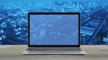 Modern dizüstü bilgisayar ekranındaki düz ikon şehir kulesi, sokak, ekspres yol ve gökdelen üzerinde ahşap masa, iş bankacılığı online konsept