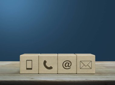 Cep telefonu, telefon, e-posta adresi, tahta blok küplerindeki posta simgesi açık mavi duvarın üzerindeki tahta masa, iş dünyası müşteri hizmetleri ve çevrimiçi destek kavramı