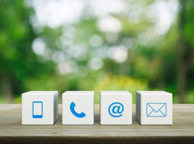 Cep telefonu, telefon, e-posta adresi ve posta simgesi beyaz blok küpleri üzerinde parktaki bulanık yeşil ağaç üzerinde ahşap masa, iş dünyası müşteri hizmetleri ve çevrimiçi konsept desteği