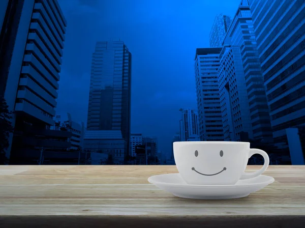 White coffee cup with smile face shape on wooden table over modern office city tower and skyscraper