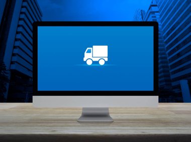 Masaüstü modern bilgisayar monitöründeki kargo kamyonu düz simgesi ofis kulesi ve gökdelen üzerinde ahşap masa, iş ulaşımı online konsept