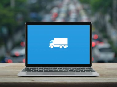 Nakliye kamyonu düz simgesi modern dizüstü bilgisayar ekranı ahşap masa üzerinde kalabalık saatte şehirde arabalar ve yollar, iş ulaşımı online konsept